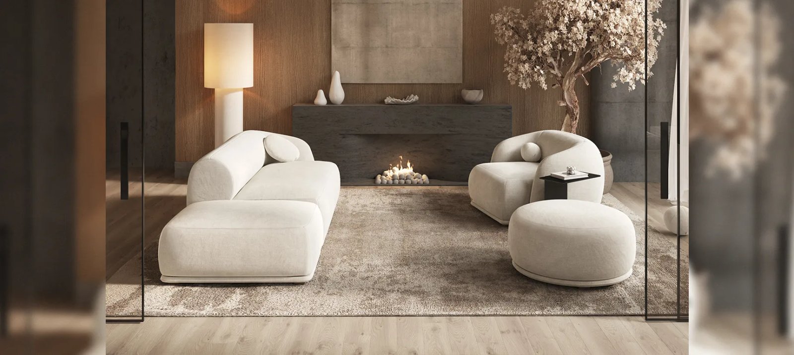 Kreminė Otis sofa ir fotelis su apgaubiančiais atlošais. Priekyje apvalintas pufas. Fone modernus židinys.