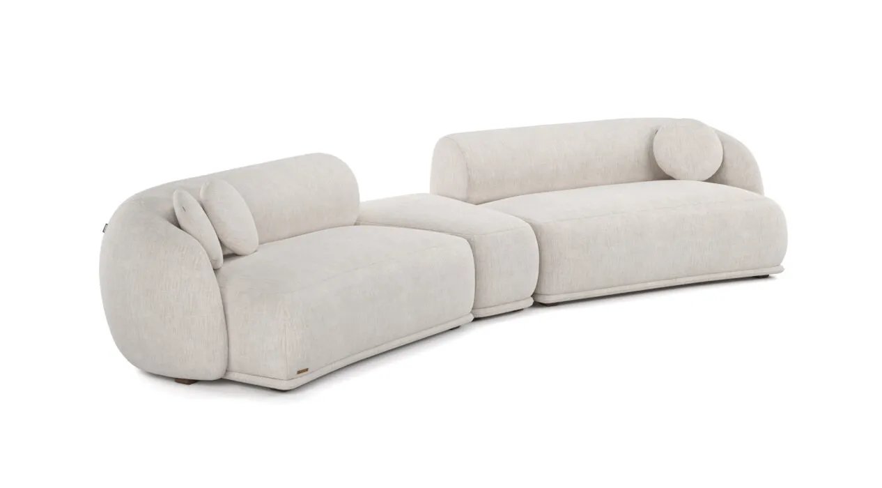 Kreminė Otis modulinė sofa iš dviejų lenktų dalių su centriniu pufu ir apvaliomis pagalvėlėmis.