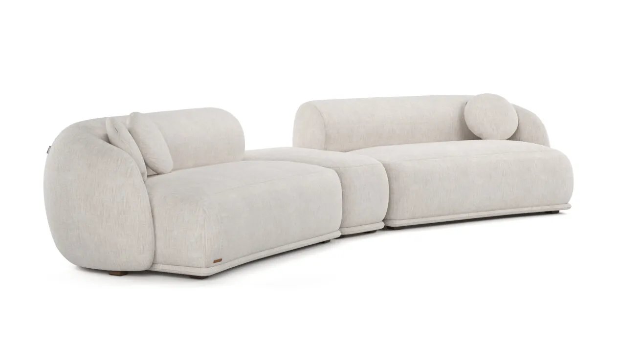 Kreminė Otis sofa iš dviejų plačių lenktų dalių su siauru jungiamuoju moduliu ir apvaliomis pagalvėlėmis.