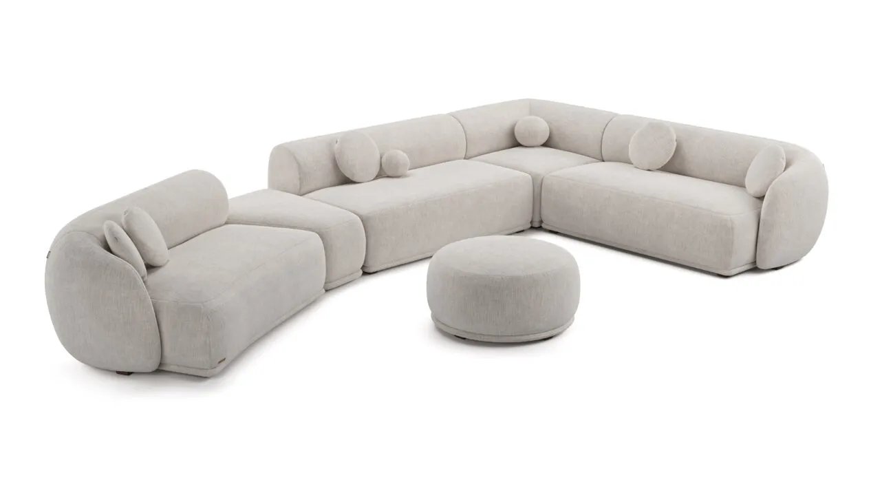 Kreminė Otis modulinė kampinė sofa su plačiu lenktu išdėstymu. Priekyje atskiras apvalus pufas.