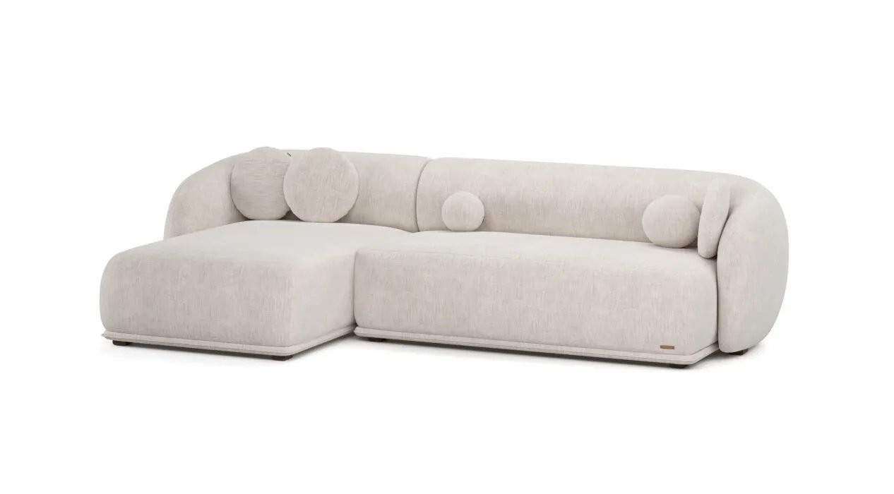 Kreminė Otis kampinė sofa su plačia kairine gulimąja dalimi ir apvaliomis dekoratyvinėmis pagalvėlėmis.