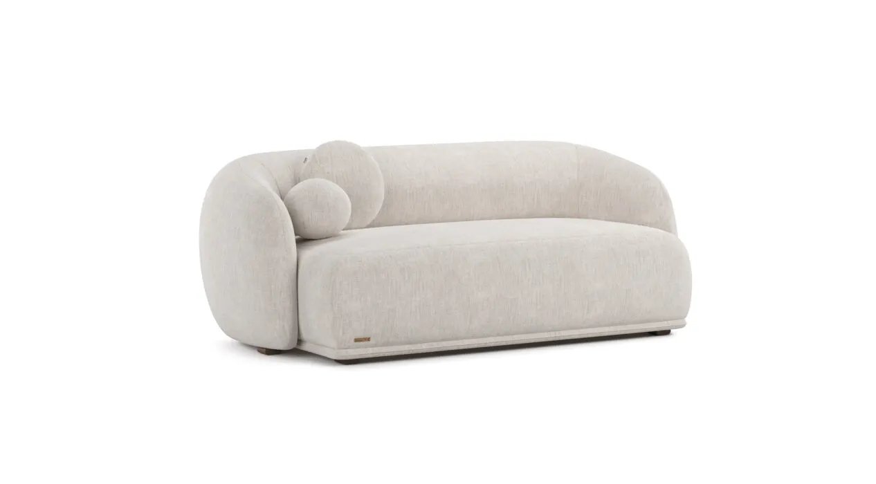 Kreminio tekstūrinio audinio Otis sofa su gilia vientisa sėdyne ir lenktu atlošu. Kairėje apvali pagalvėlė.