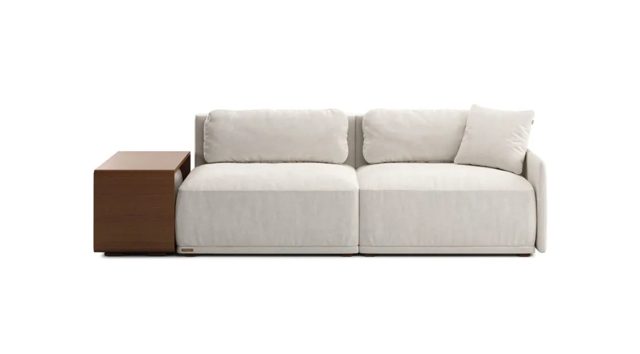 Tiesi kreminė Cruse sofa su dviem plačiomis sėdynėmis ir trimis minkštomis pagalvėmis. Kairėje rudas staliukas.