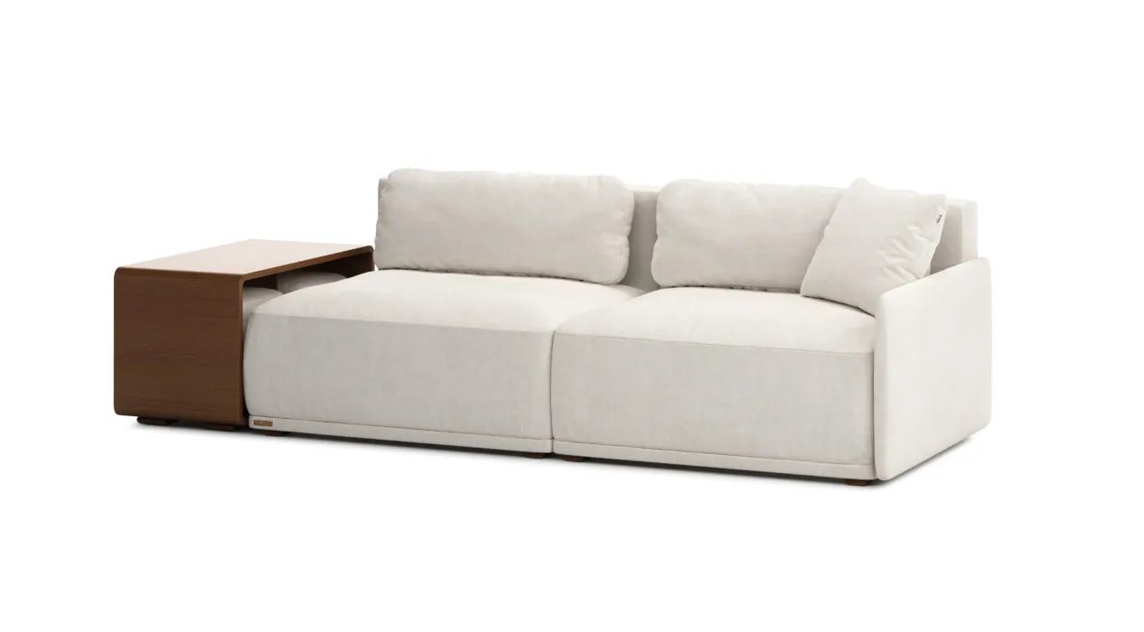 Kreminė Cruse sofa su dviem plačiomis sėdynėmis ir minkštomis nugaros pagalvėmis. Kairėje integruotas rudas staliukas.